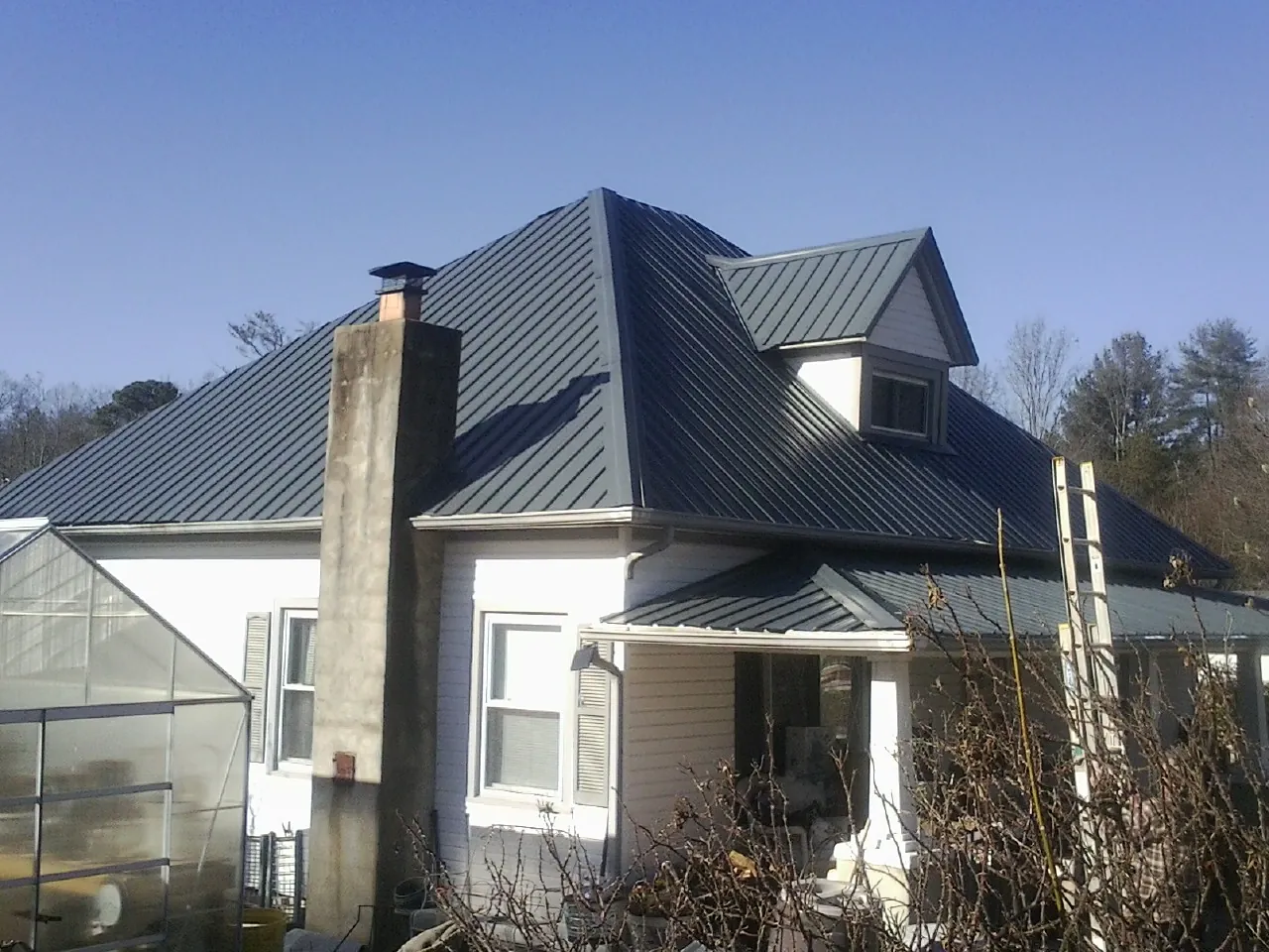 Dark blue standing seam metal roof on a white farmhouse with dormer — Slate & Tile Roof Repair by Roofing Brothers in Cornish